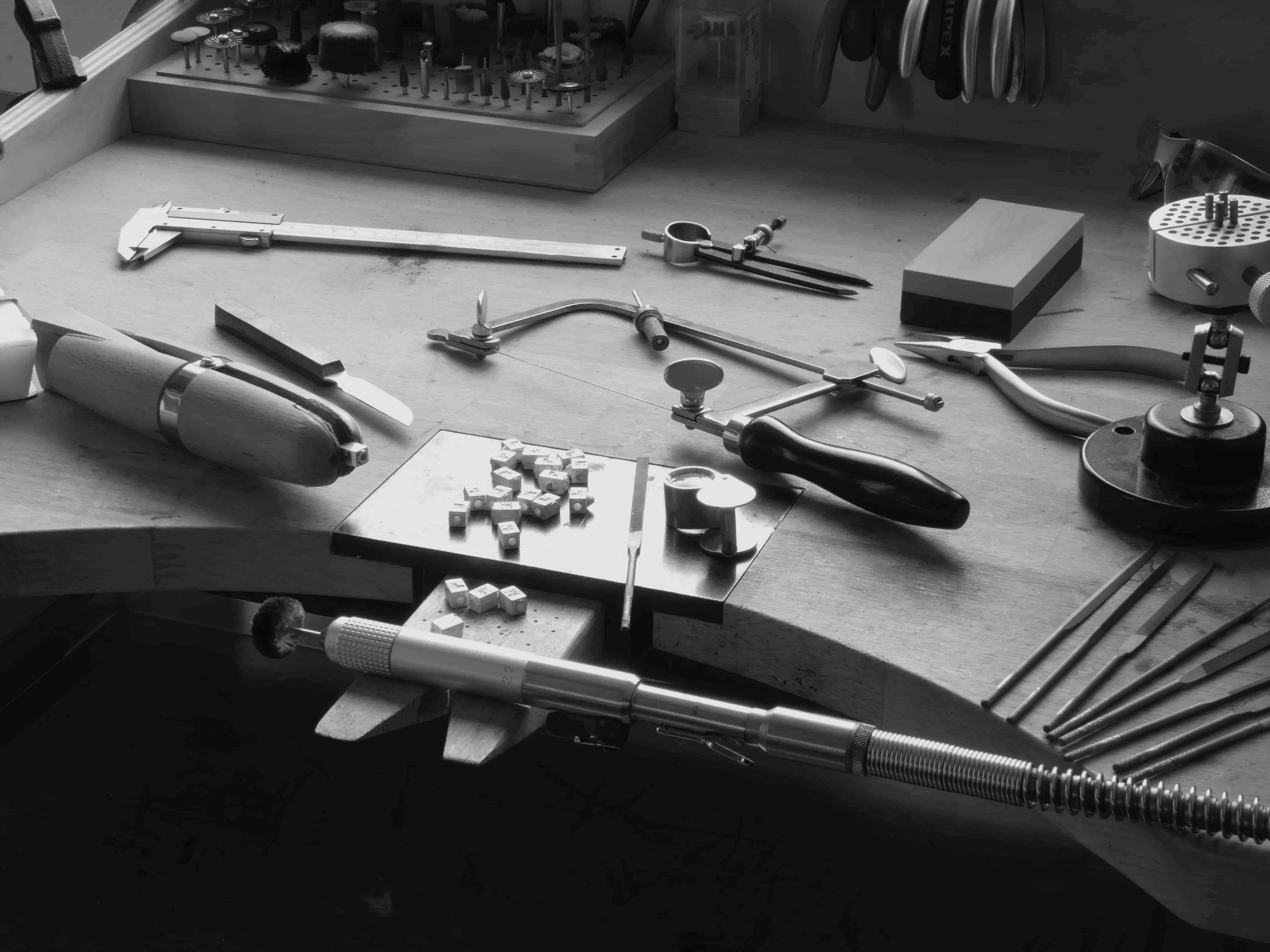 goudsmit bureau met een loep en diverse vijlen, tangen, hangmotor, zaag en zilveren voloria leeuw logo kubus zwart wit foto